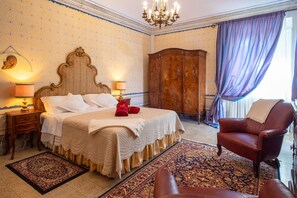 A hotel room with a large bed, a wooden wardrobe, a leather armchair, and a chandelier.