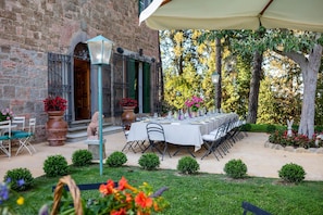 An outdoor dining area with a long table set for a meal, surrounded by greenery and a brick building. - Tenuta Bartolucci - Ten Bedroom Villa, Sleeps 22 (Palaia)