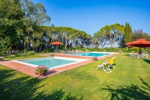 A pool area with two pools, surrounded by grass and trees.