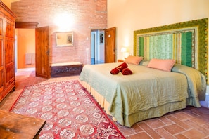 A bedroom with a brick wall, a wooden wardrobe, a bed with a green headboard, and a patterned rug. - Tenuta Bartolucci - Ten Bedroom Villa, Sleeps 22 (Palaia)