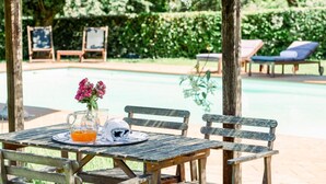 Une table en bois sur laquelle se trouvent une carafe de jus d’orange, une serviette blanche pliée et des fleurs roses.