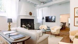 Un salon avec une cheminée, un canapé, deux fauteuils, une table basse et un téléviseur fixé au mur.