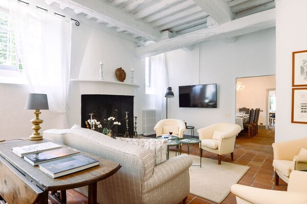 Un salon avec une cheminée, un canapé, deux fauteuils, une table basse et un téléviseur fixé au mur.