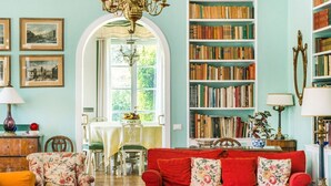 Un salón acogedor con un sofá rojo, sillones estampados, una mesita de centro y una estantería llena de libros.