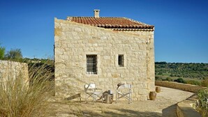 A stone building with a tiled roof, two windows, and a small patio with chairs and a table. - La Picca Estate - Six Bedroom Villa, Sleeps 12 (Scicli)
