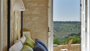 A bedroom with a stone wall, a bed with pillows, a white lamp, and an open door leading to a balcony with a view of the countryside. - La Picca Estate - Six Bedroom Villa, Sleeps 12 (Scicli)
