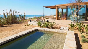 Ett modernt hus med en glasfasad, en pool och en uteplats med utsikt över stranden.