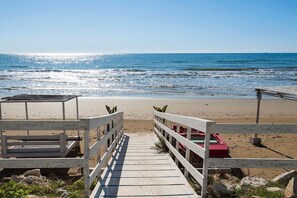 A wooden pier leading to a beach with a red boat parked on the sand.