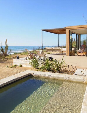 A modern outdoor lounge area with a pool, seating, and a view of the ocean.