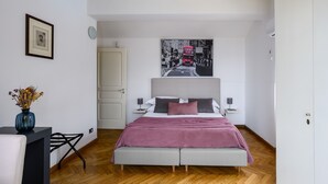 A bedroom with a bed, a nightstand, a lamp, a framed picture, and a vase with flowers. - Villa Naxos - Eight Bedroom Villa, Sleeps 18 (Taormina)