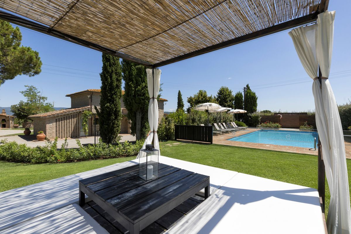 A covered outdoor seating area with a pool in the background.