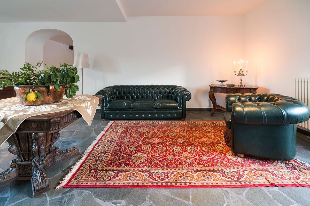 A living room with a dark green sofa, a matching ottoman, a patterned rug, a wooden coffee table with a plant, and a lamp.
