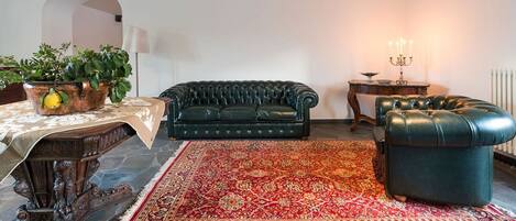 A living room with a dark green sofa, a matching ottoman, a patterned rug, a wooden coffee table with a plant, and a lamp.
