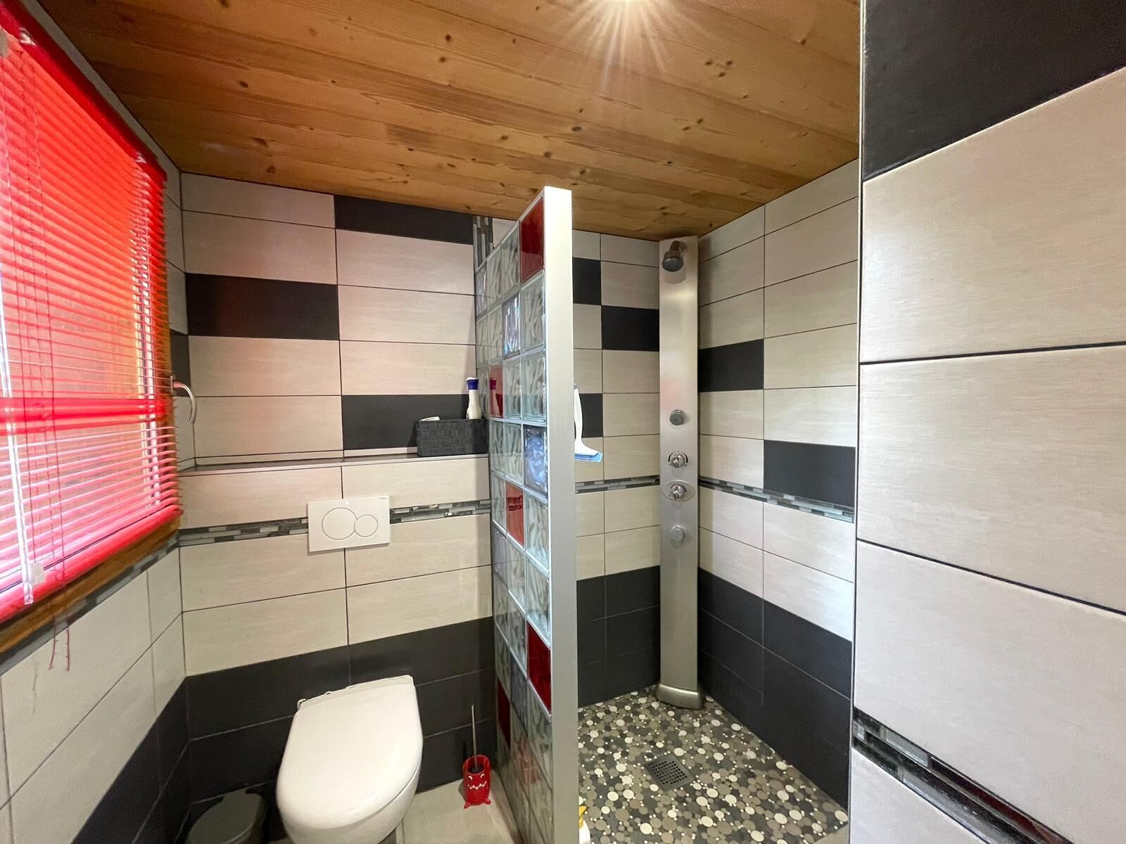 A compact bathroom with a shower, toilet, and a small storage area.