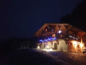 A rustic chalet with a wooden exterior, a balcony, and string lights.