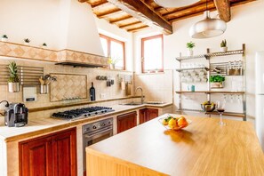 Eine moderne Küche mit einer zentralen Kochinsel, einem Herd, Backofen und Spüle. Verschiedene Küchenutensilien und Geräte sind vorhanden, darunter eine Kaffeemaschine und eine Weinflasche.