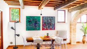 Een eethoek met een houten tafel, transparante stoelen en twee abstracte schilderijen aan de wand.