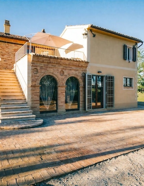 Un bâtiment à deux étages avec une façade en briques, un balcon surmonté d’un auvent beige et un escalier menant à l’entrée.