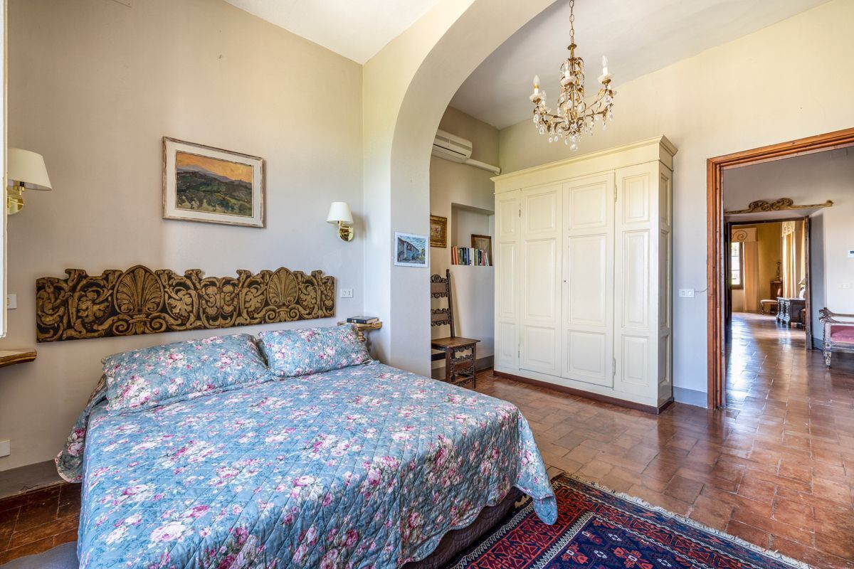 A bedroom with a large bed, a chandelier, a wardrobe, and a painting on the wall.