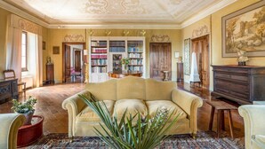 Amplia habitación con un sofá color beige, una estantería grande y un diseño de techo clásico.