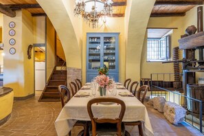 A dining area with a long table set for six, surrounded by chairs, a chandelier, and a blue cabinet with glassware. - Torre La Marmora - Four Bedroom Apartment, Sleeps 8 (Otricoli)