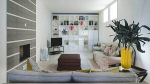 Un salon moderne avec un canapé gris, un téléviseur et une bibliothèque remplie de divers objets.