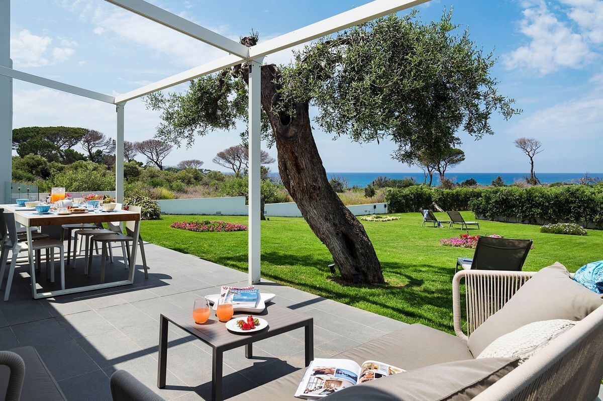 Un espace extérieur abrité, aménagé pour prendre les repas, avec une table pour deux, un canapé et un magazine posé sur le sol.