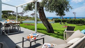 Un espace extérieur abrité, aménagé pour prendre les repas, avec une table pour deux, un canapé et un magazine posé sur le sol.