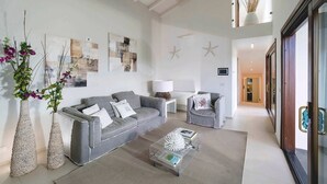 Un salon moderne avec un canapé gris, deux fauteuils, une table basse et des éléments décoratifs, comme des étoiles de mer accrochées au mur et un vase rempli de fleurs.
