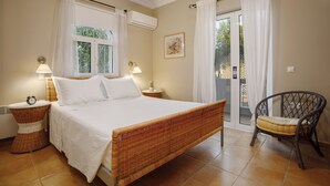 Une chambre à coucher avec un lit, des lampes de chevet, un fauteuil en osier et une fenêtre avec des rideaux.