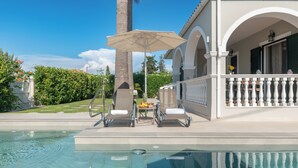 Un espace piscine équipé de chaises longues, d’un parasol et offrant une vue sur un immeuble doté d’un balcon.