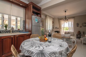 Una cocina con armarios de madera, un refrigerador, una mesa de comedor con mantel de hojas tropicales y un frutero.