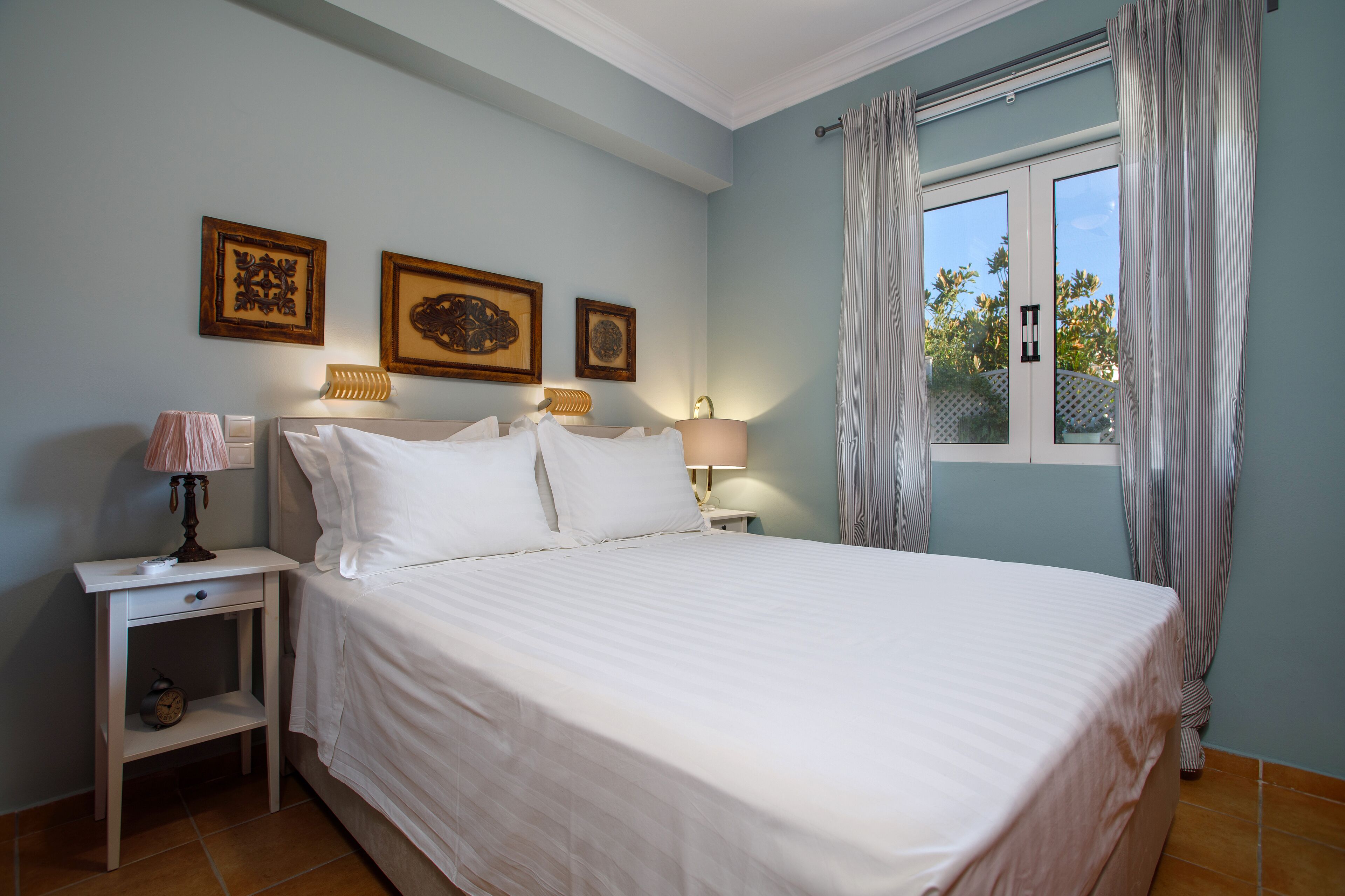 A neatly made bed in a room with light blue walls, two bedside tables with lamps, and three framed pictures on the wall.