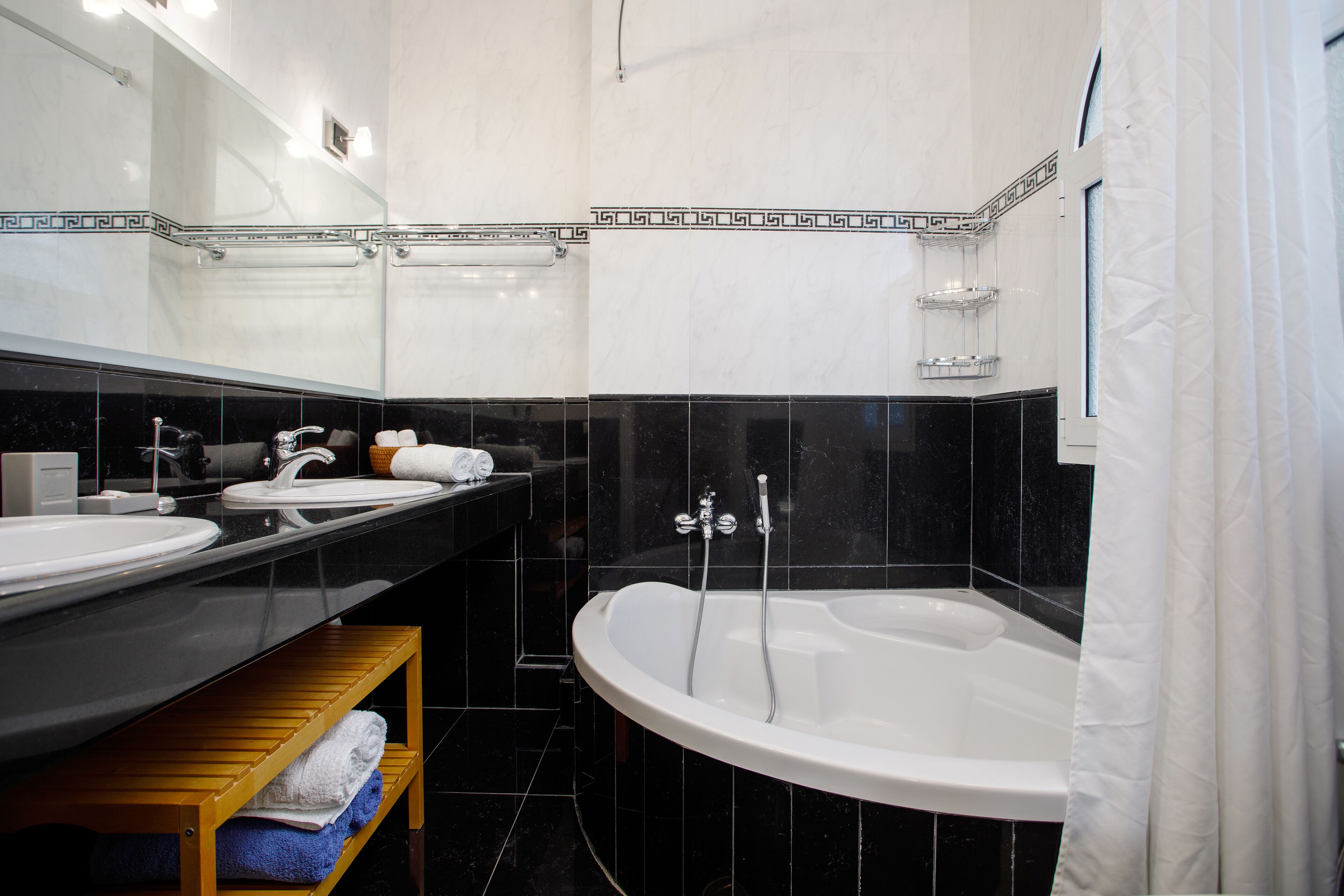 Une salle de bain moderne avec une baignoire sur pieds, deux vasques et une étagère en bois où sont posées des serviettes.