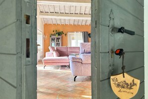 A cozy living room with a pink sofa and armchair, a wooden door with a keyhole, and a tiled floor.