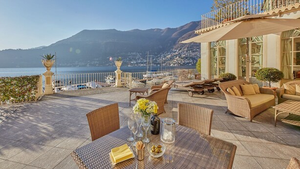 Eine Terrasse mit Korbmöbeln, einem Esstisch und Blick auf das Meer und die Berge.