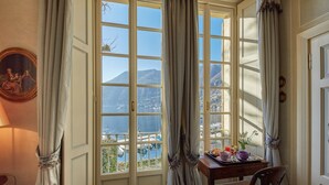 Ein Zimmer mit großem Fenster und Blick auf eine gebirgige Landschaft sowie ein Gewässer.
