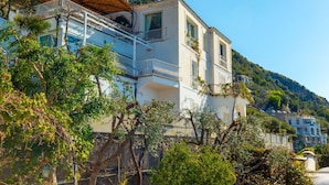 Ein zweistöckiges Gebäude mit Balkonen, umgeben von üppiger Vegetation und einer Bergkulisse.