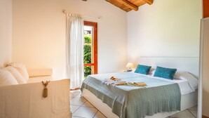 Ein Schlafzimmer mit Bett, Nachttisch, Fenster mit Vorhängen und Holzboden.
