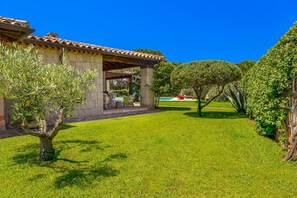 A stone building with a tiled roof, a covered patio with chairs, and a well-maintained lawn. - Domus De Acacia - Three Bedroom Villa, Sleeps 6 (San Teodoro)