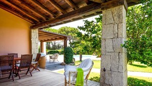 Eine Terrasse im Freien mit Holzboden, einer Steinsäule und einem überdachten Sitzbereich mit Stühlen und Tisch.