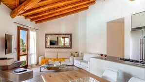 Ein modernes Wohnzimmer mit Holzboden, weißen Sofas, einem Esstisch und einer Küchenzeile inklusive Kühlschrank.