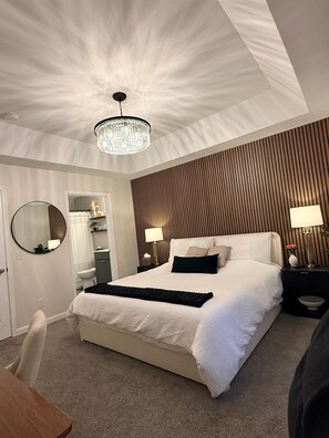 Un dormitorio de hotel moderno con una cama grande, un candelabro, un espejo redondo y una pared revestida de madera.