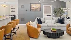 A modern living room with a grey wall, a sofa, a coffee table, and a bar area with stools.