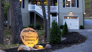 A wooden sign with a mountain silhouette and the text 'Treviño's Getaway Est. 2022' in front of a two-story house with a balcony and a garage.