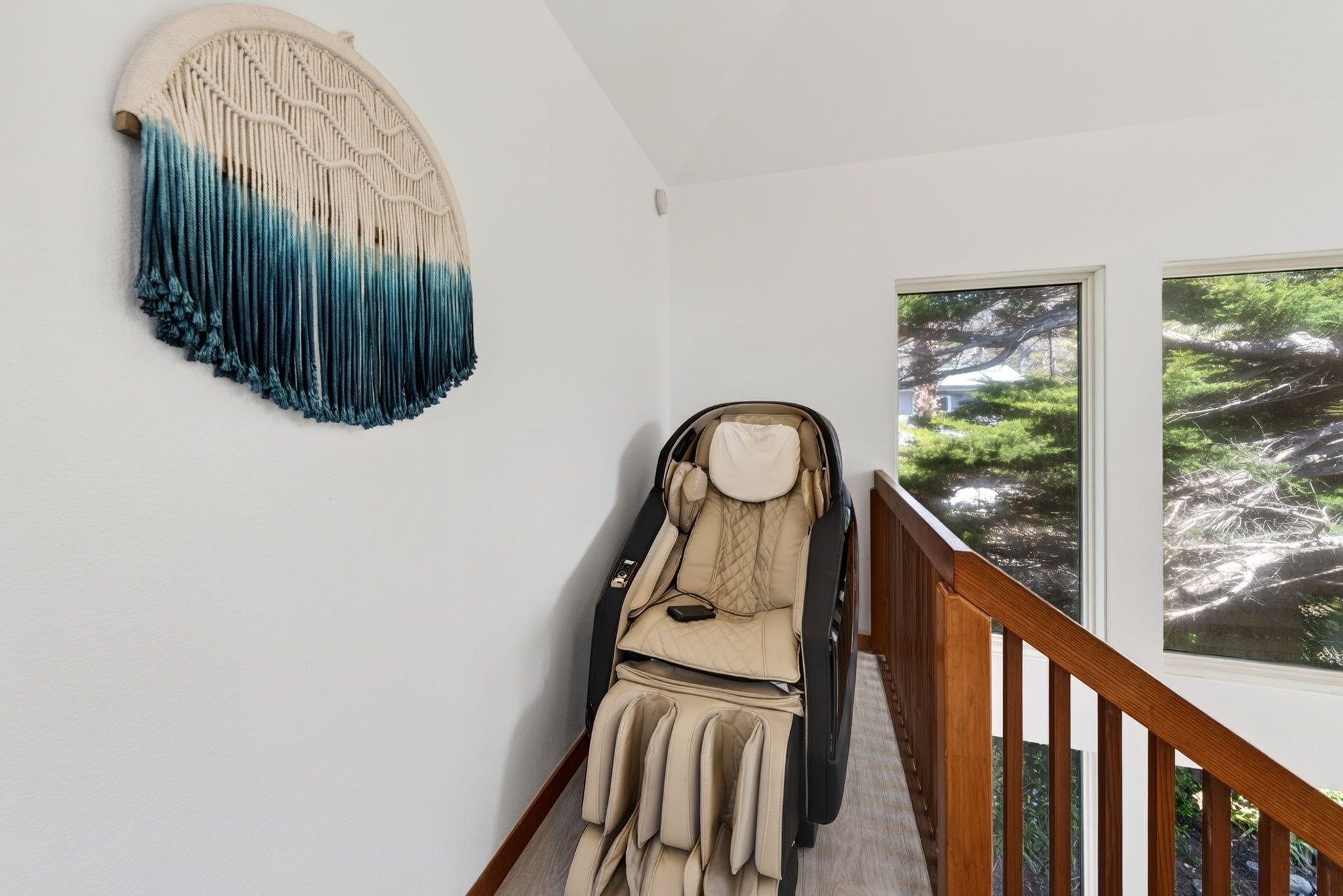 A massage chair in a room with a large window, a wall-mounted macrame piece, and a wooden staircase.