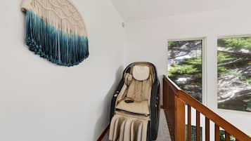 A massage chair in a room with a large window, a wall-mounted macrame piece, and a wooden staircase.