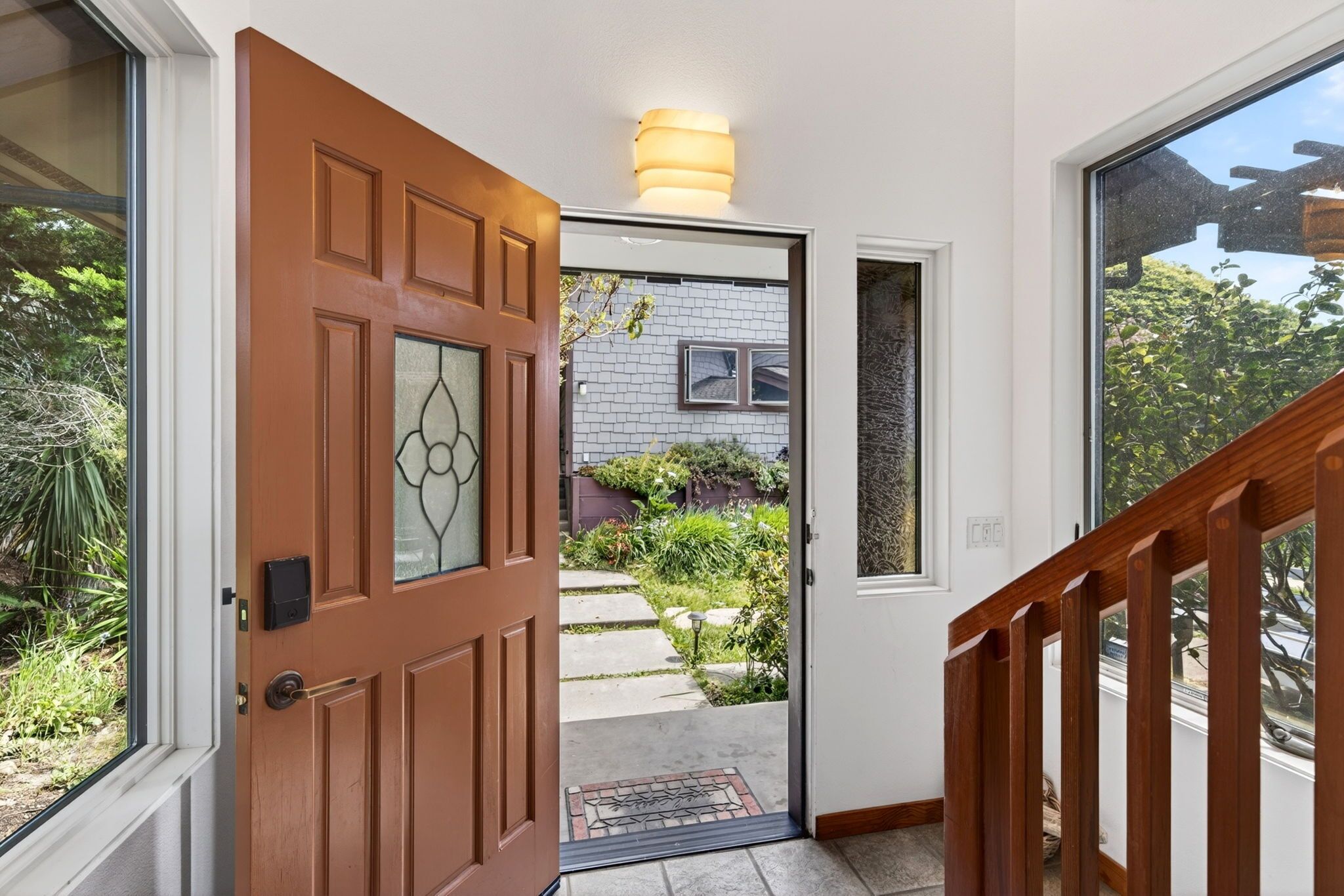 A wooden door leading to a garden with a stone pathway, a small window, and a light fixture above the door.