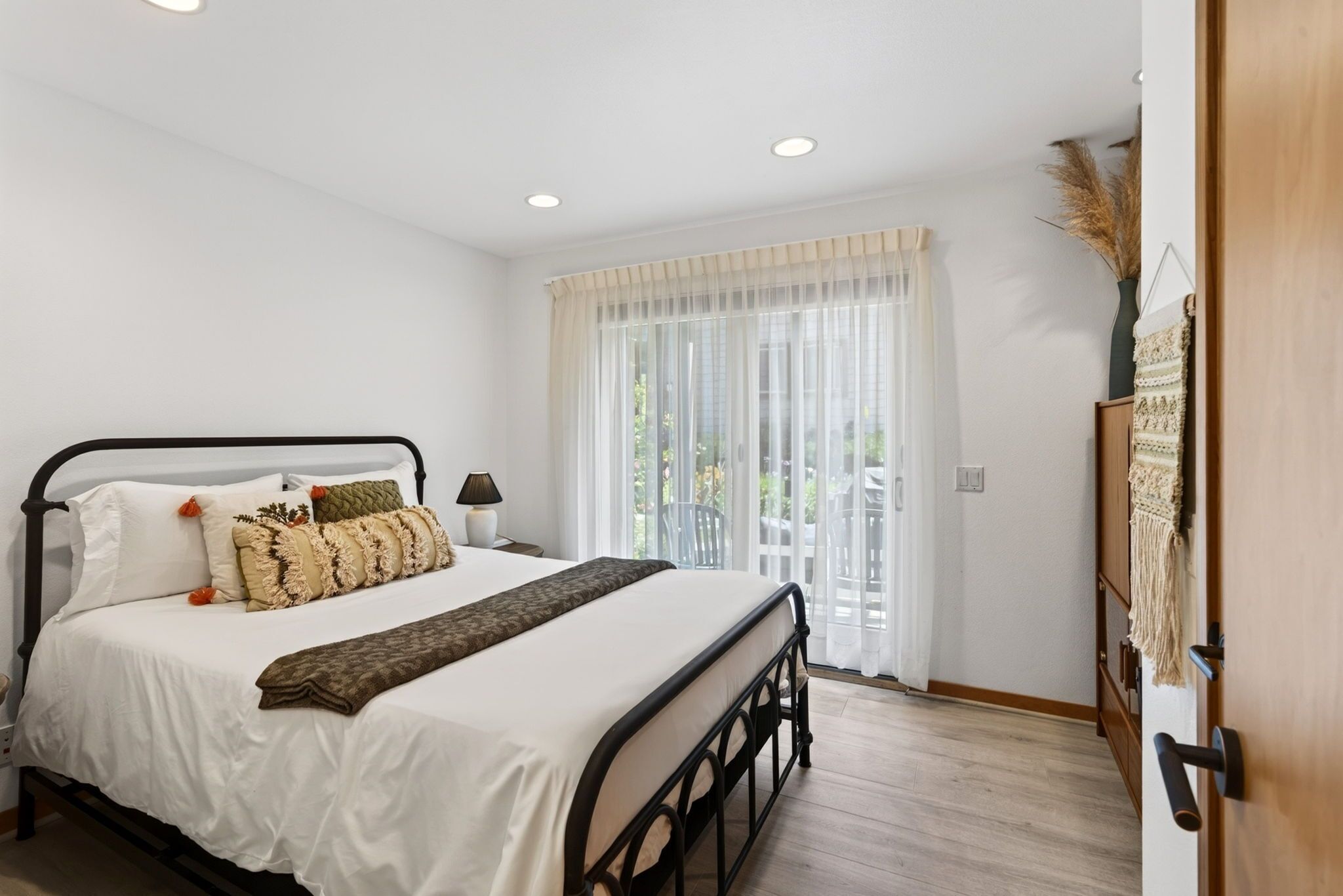 A bedroom with a bed, bedside table, lamp, and a view of the outdoors through a window.