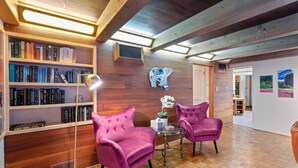 Une bibliothèque avec des étagères, deux fauteuils violets, une petite table avec une lampe et une décoration murale représentant des papillons.